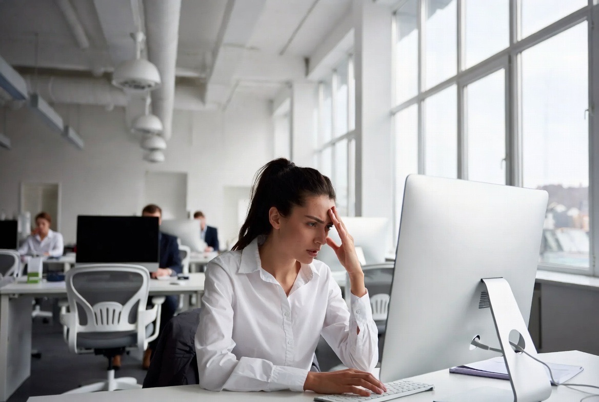 A stressed professional at a desk reviewing information on a monitor